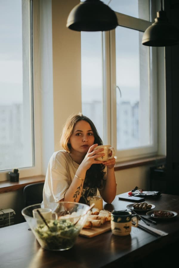 A woman sitting at a table at home with a mug of coffee.