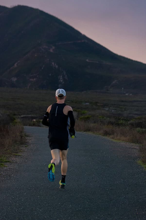 A runner on a road through open hill country, seen from behind.